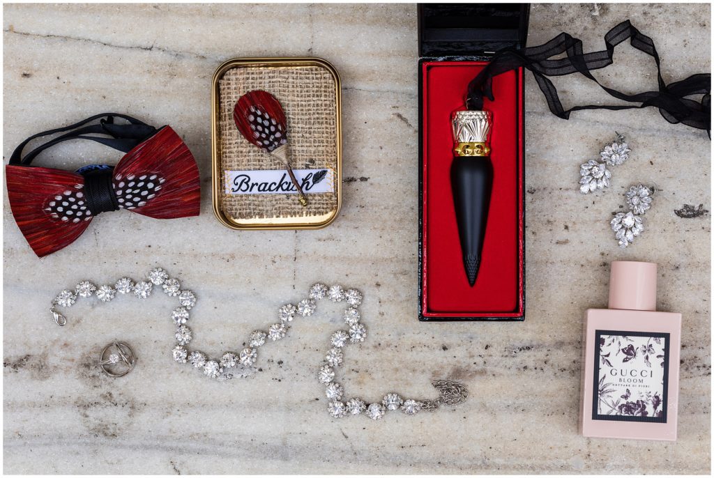 Bride and grooms details on marble background, including featuring bow tie and boutonniere