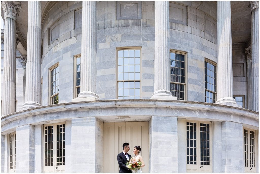 wide angle portrait of bride and groom in front of marble building