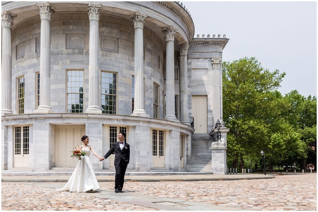 groom leading bride down a path in front of a marble building