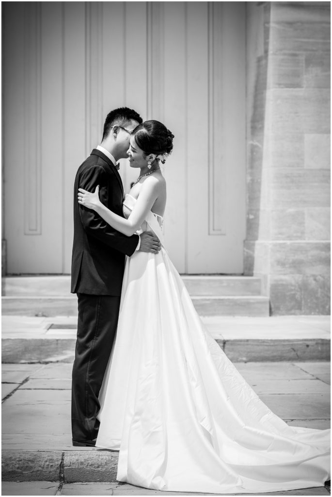 black and white portrait of bride and groom, groom whispering into brides ear