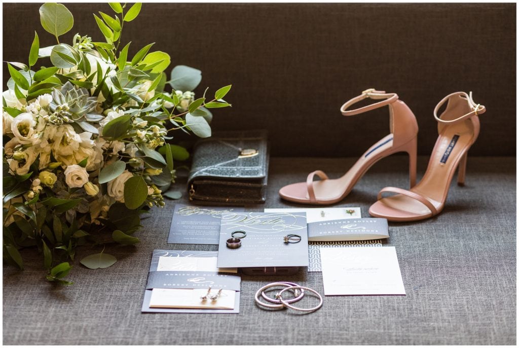 Bridal details at the Cambria Hotel, including bouquet with white flowers and greens, and invitation suite with charcoal and gold