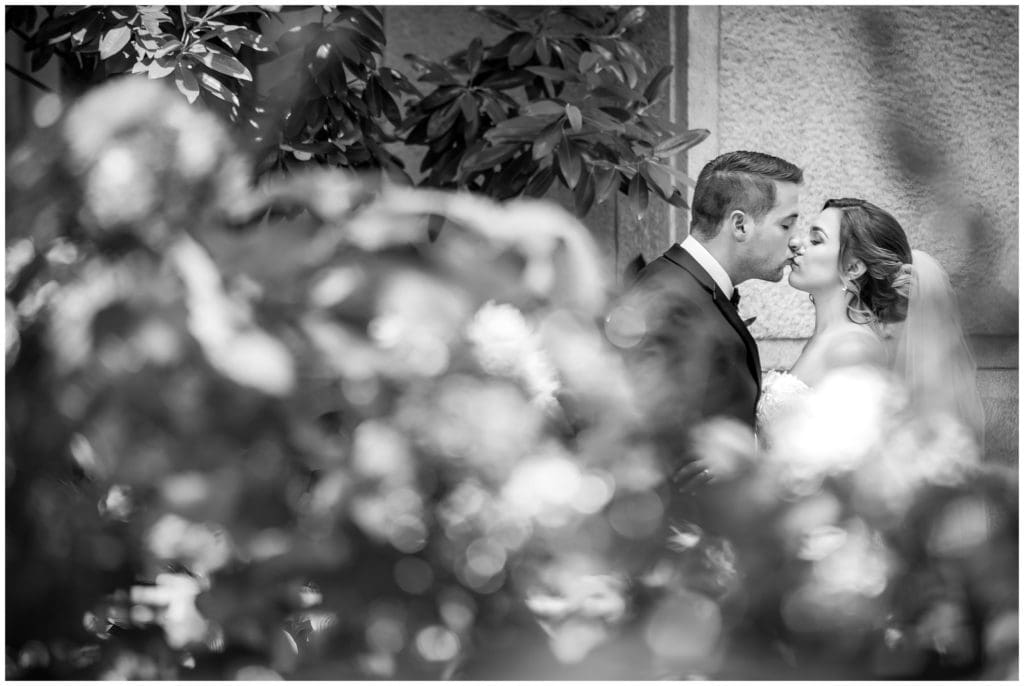 black and white portrait of bride and groom kissing through flowers at City Hall