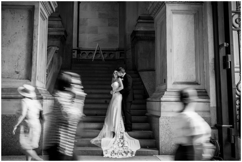black and white portrait of bride and groom at City Hall with people passing through