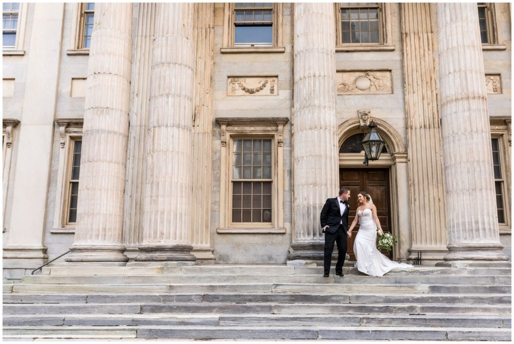 Outdoor portrait of bride and groom walking down marble stairs together before their wedding at the Lucy by Cescaphe
