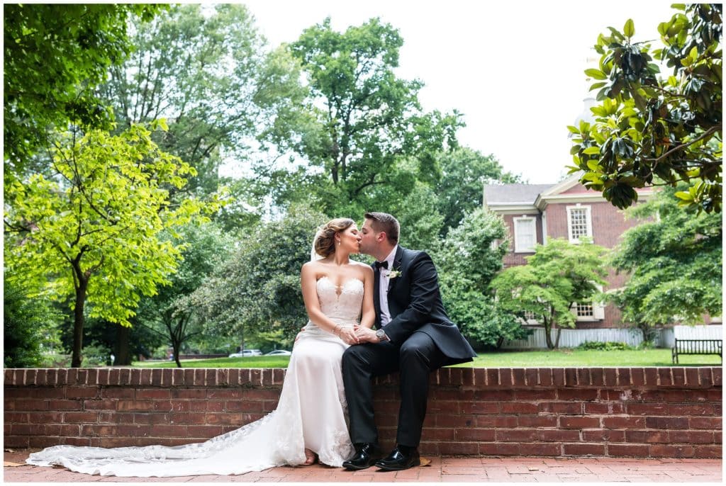 Romantic outdoor portraits of bride and groom sitting on a brick wall in front of greenery
