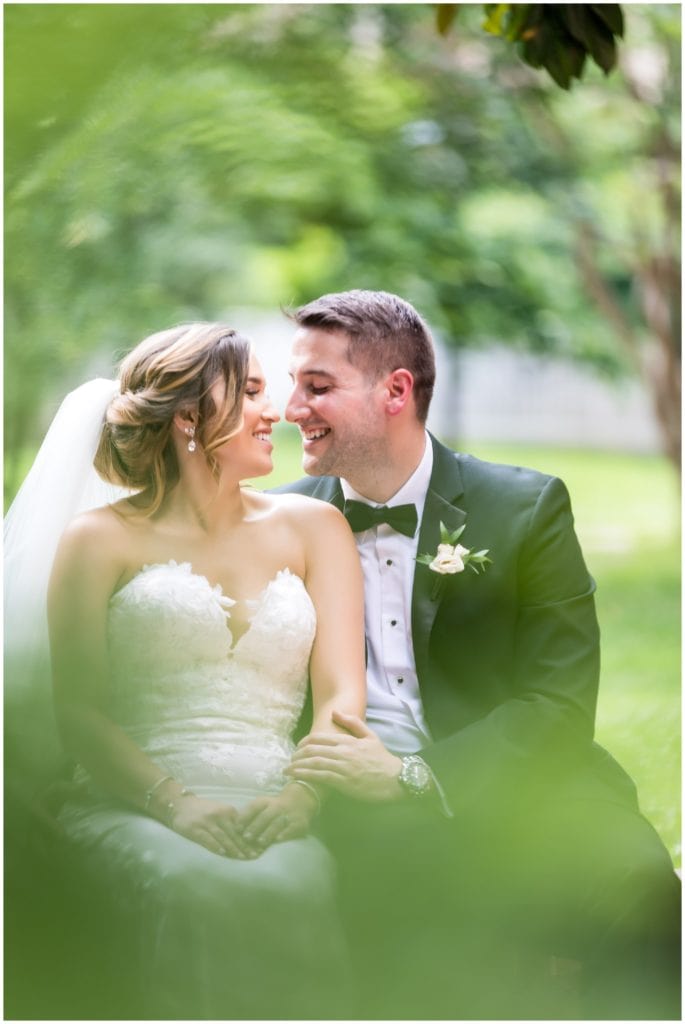 Romantic outdoor portraits of bride and groom sitting on a brick wall shot through greenery