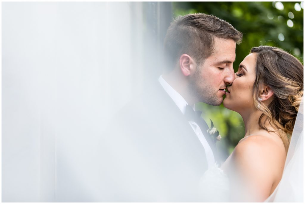 Romantic outdoor portrait through the veil of bride and groom almost kissing