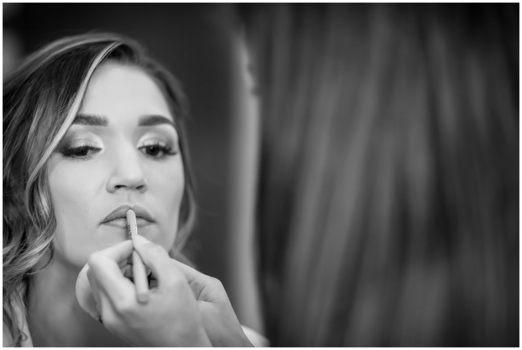 black and white portrait of bride having her lipstick applied at the Cambria Hotel before wedding at The Lucy by Cescaphe