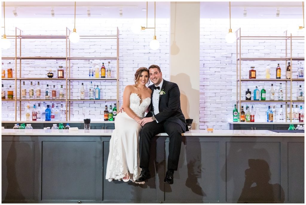 bride and groom sitting on the bar at their wedding reception in The Lucy by Cescaphe