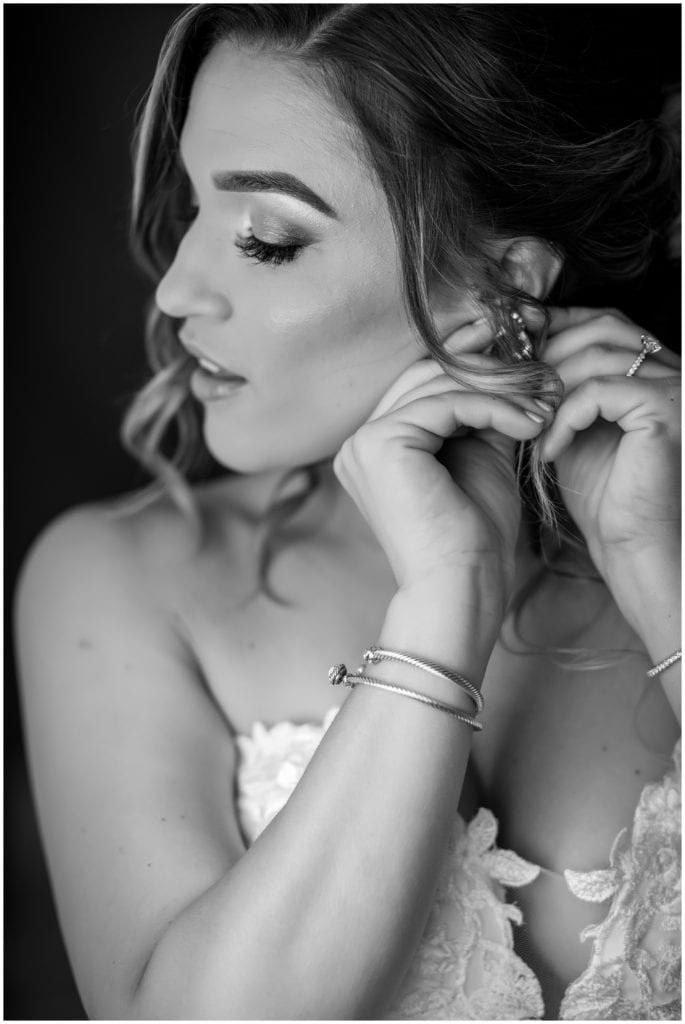 black and white portrait of bride putting her earrings on before her wedding at the Lucy by Cescaphe