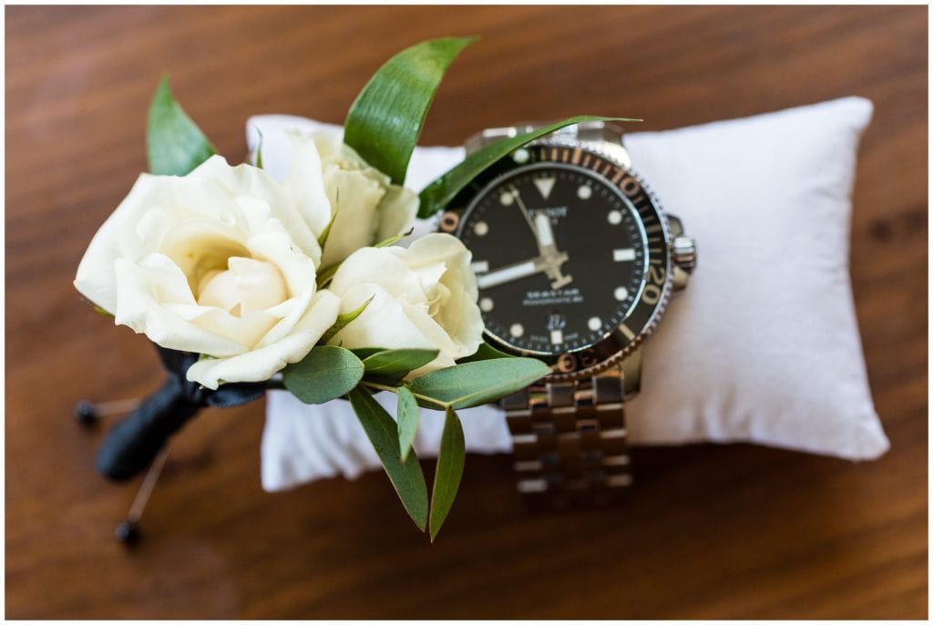 Detail of grooms white rose and greens boutonniere and watch on pillow at the Cambria Hotel