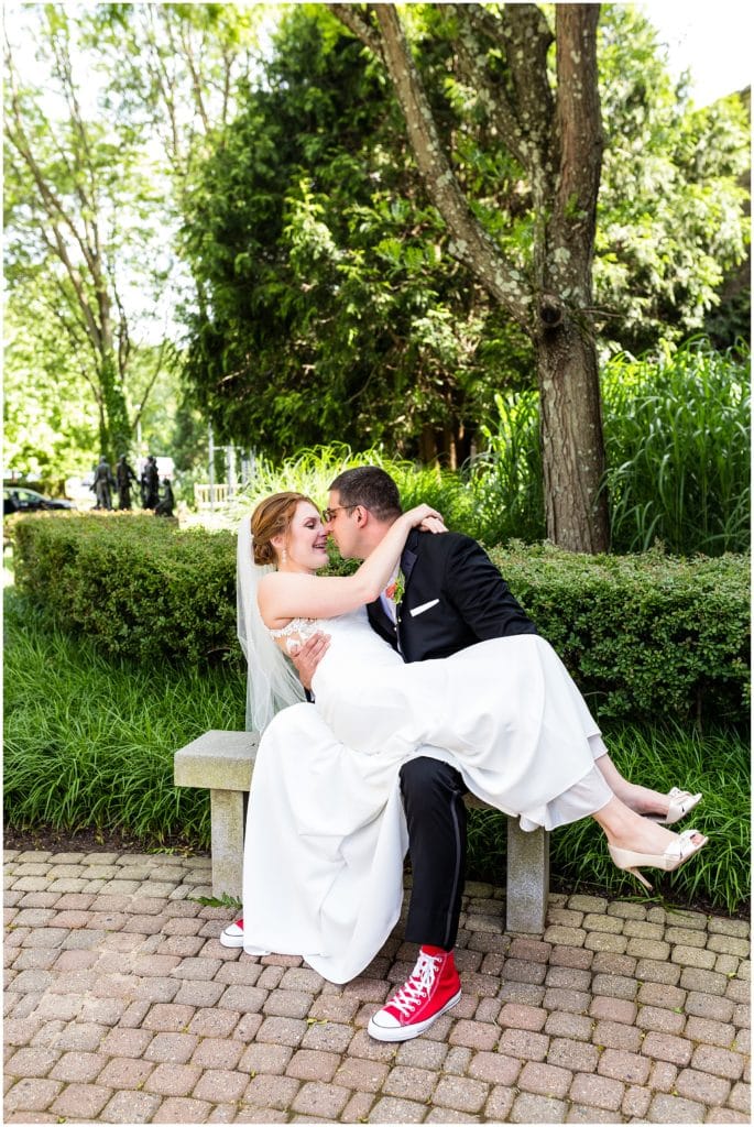 Groom holding bride on his lap while sitting on a bench in the courtyard of the Michener Museum