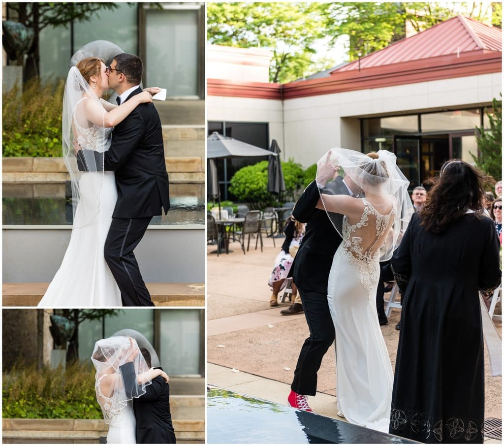 Bride and groom sharing their first married kiss - groom cheekily pulling bride's veil over their heads to hide