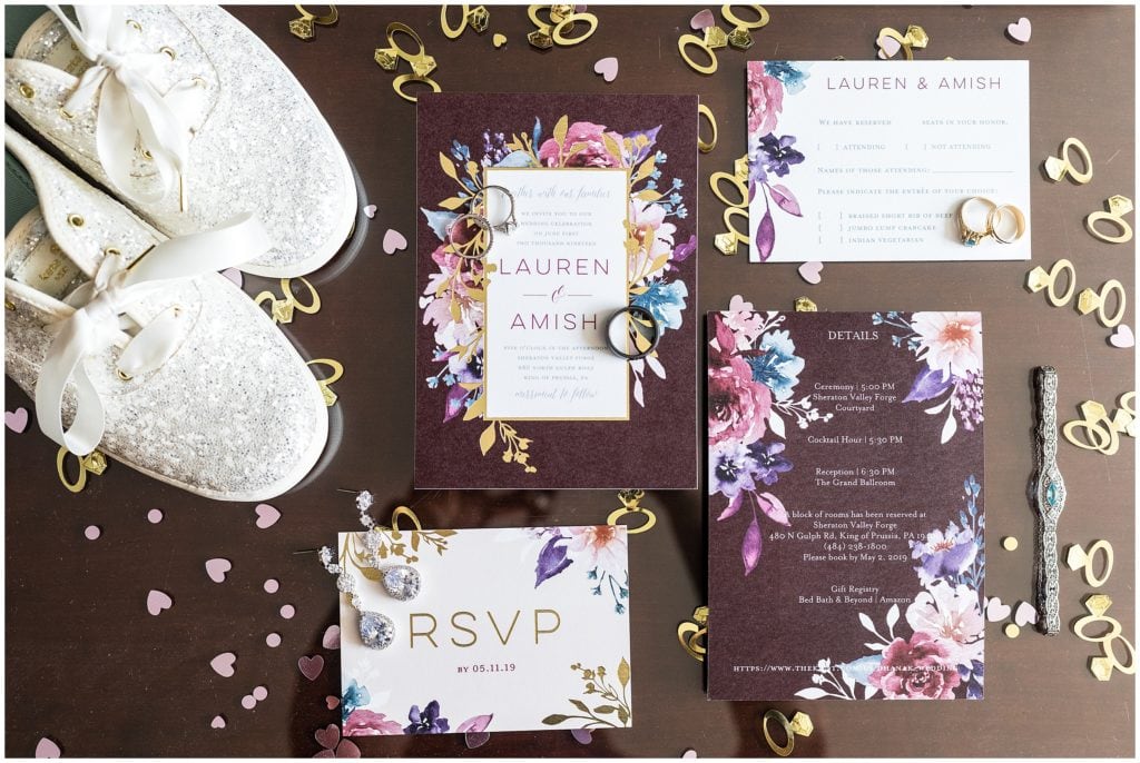 floral purple wedding invitation flat lay with jewelry, shoes, and confetti