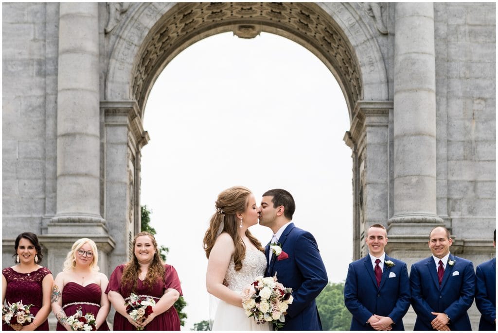 bride and groom kissing with bridal party at Valley Forge Park Archway