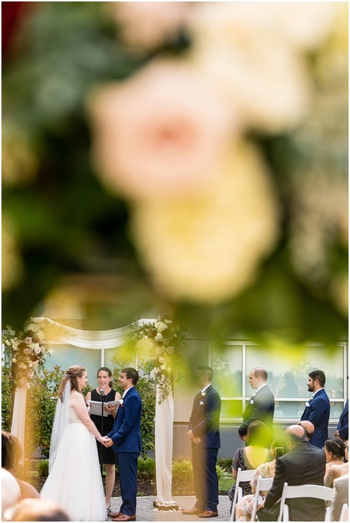 wedding ceremony bride and groom shot through florals with interesting perspective
