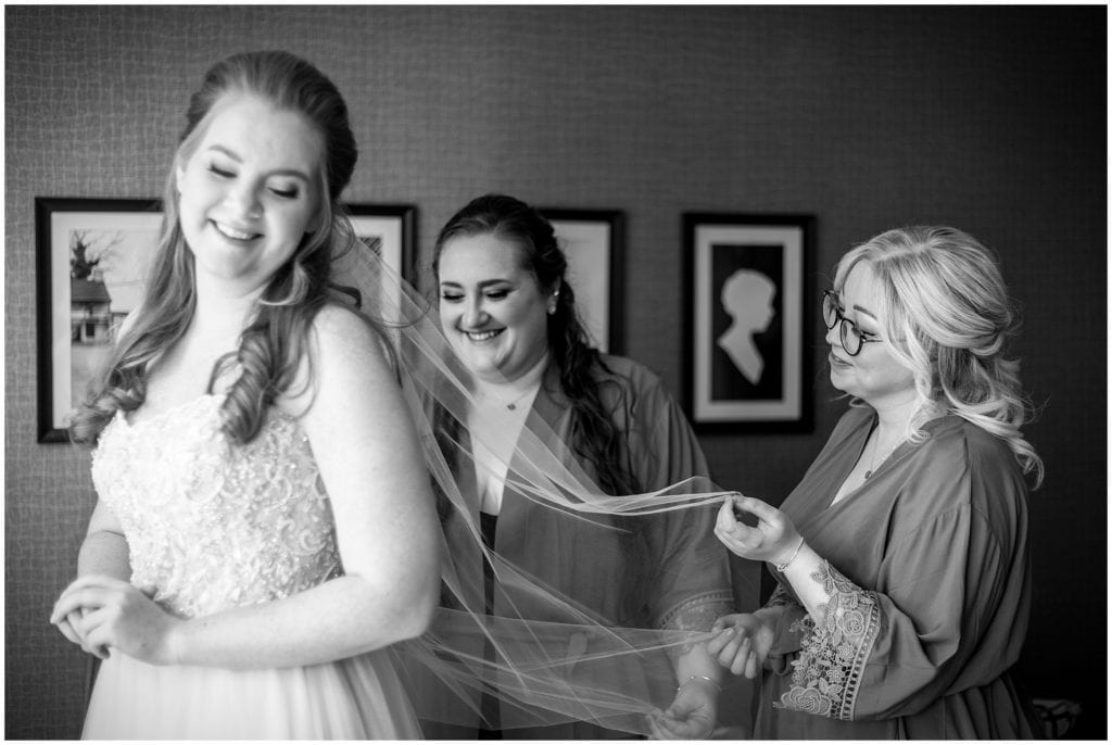 elegant black and white portrait of bridal party helping the bride with her veil