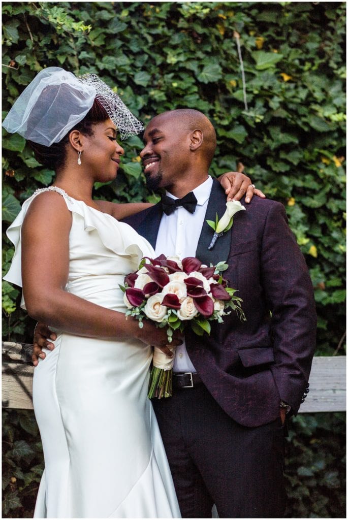 Bride and groom wedding portraits with maroon and white bouquet in front of ivy wall