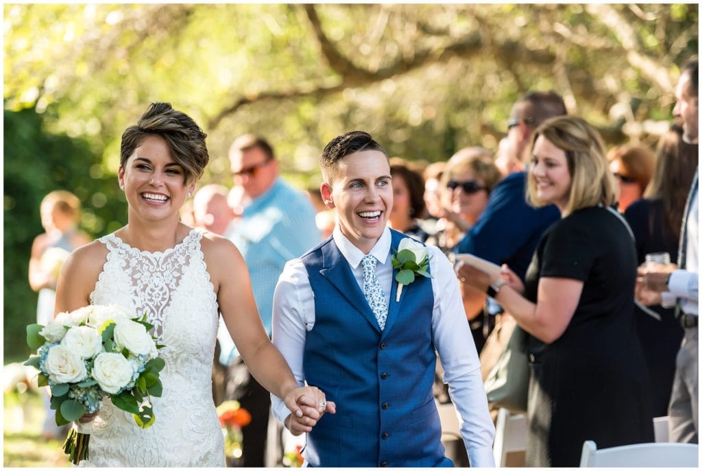 LGBT wedding brides walking up aisle together post ceremony