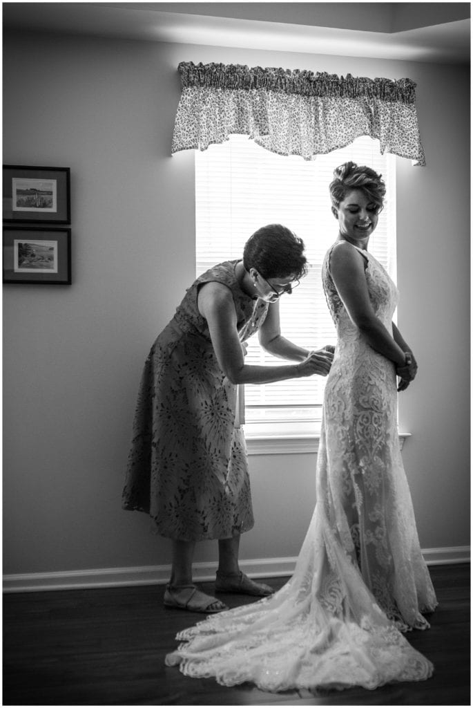 Black and white portrait of the mother of the bride buttoning brides gown