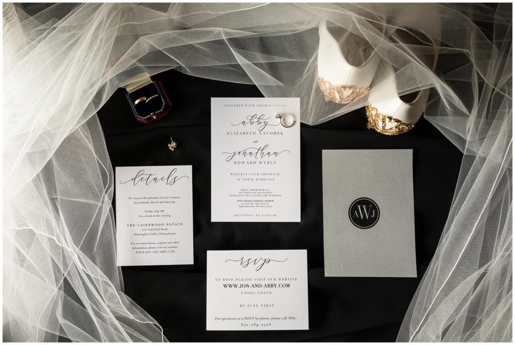 Wedding invitation suite layout with earrings, wedding bands, shoes, and veil