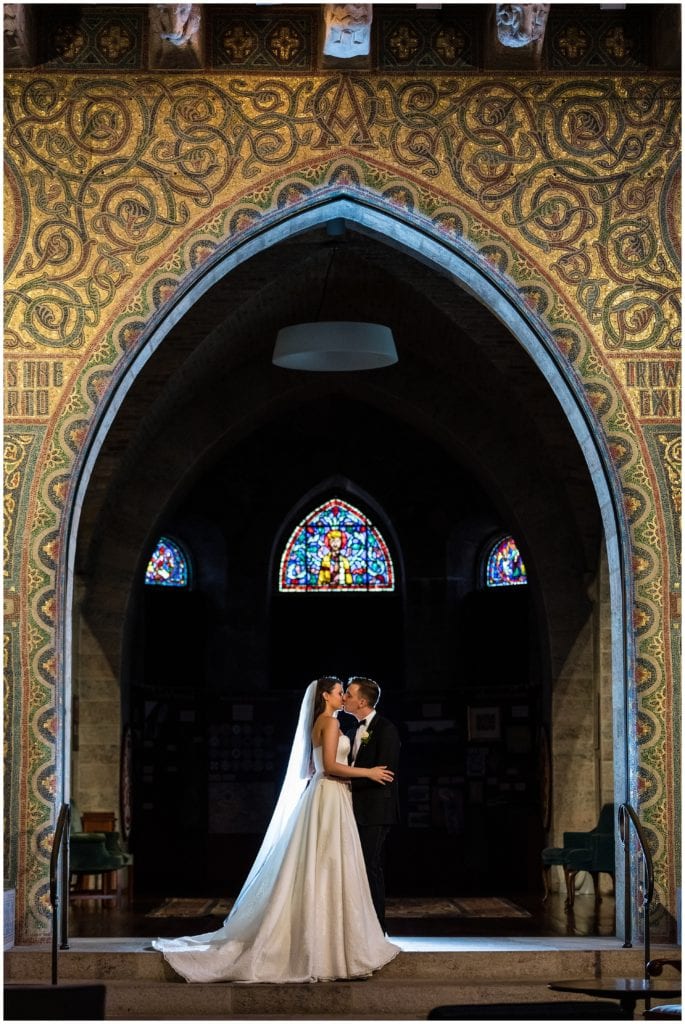 Bride and groom kissing under arch in Holy Cross Catholic Church