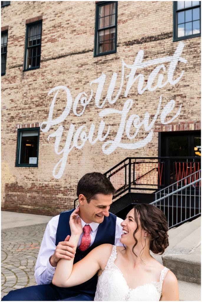 Bride and groom laughing with each other in front of "do what you love" mural in Philadelphia wedding