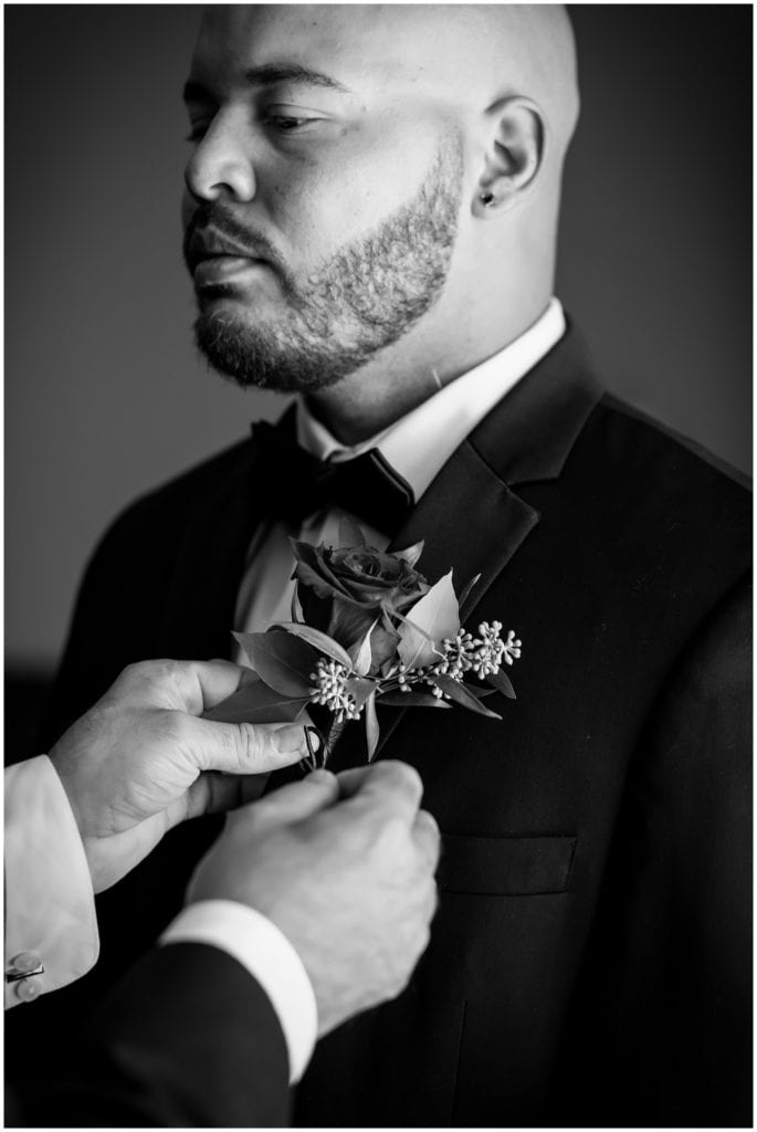 Black and white groom portrait getting boutonniere pinned