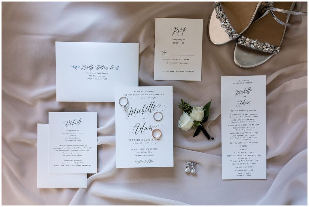 Simple black and white wedding invitation suite with wedding rings, earrings, shoes, and florals