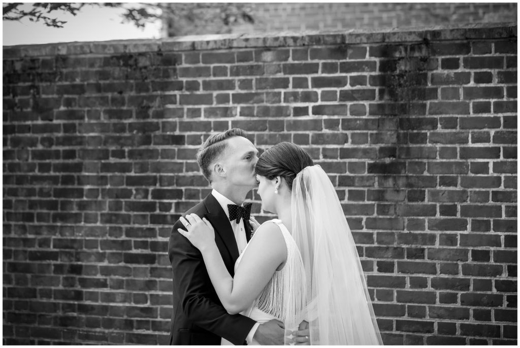 Black and white portrait with groom kissing bride on the forehead after first look