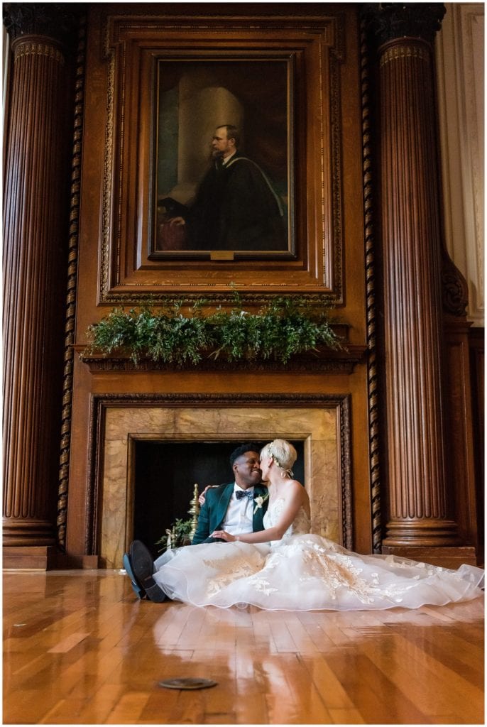Bride and groom portrait snuggled up in front of fireplace inside library