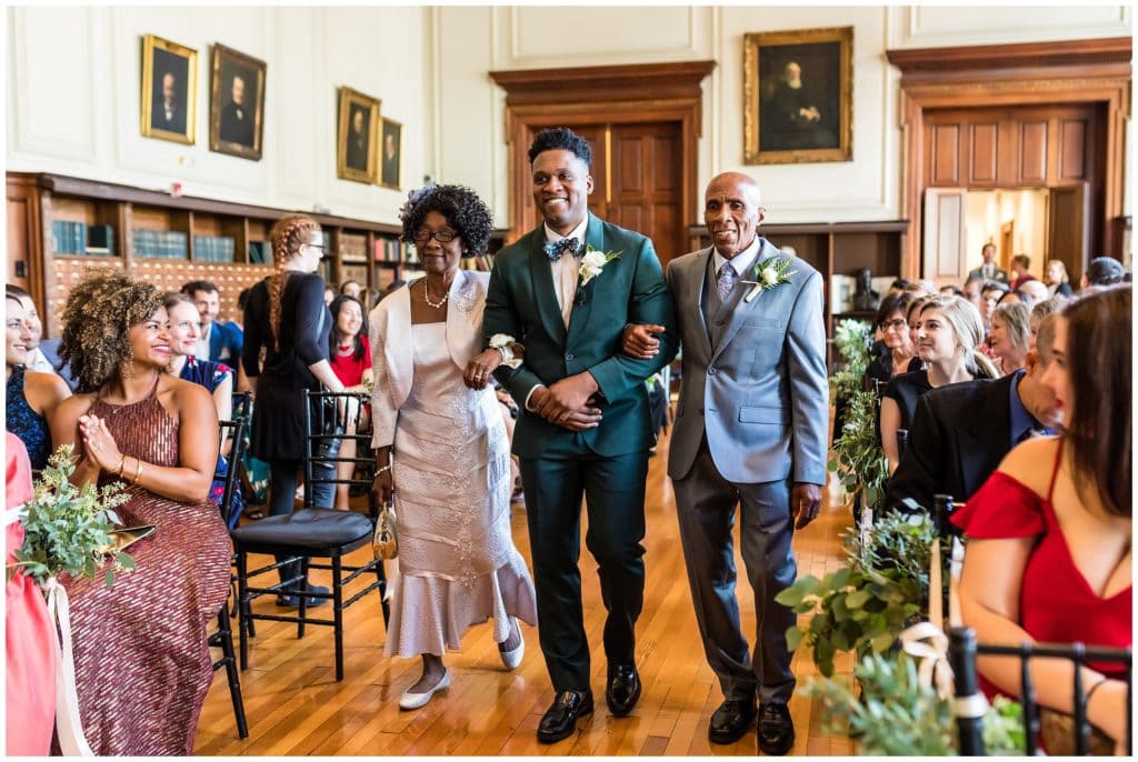 Groom walking down the aisle with his parents for indoor library wedding ceremony