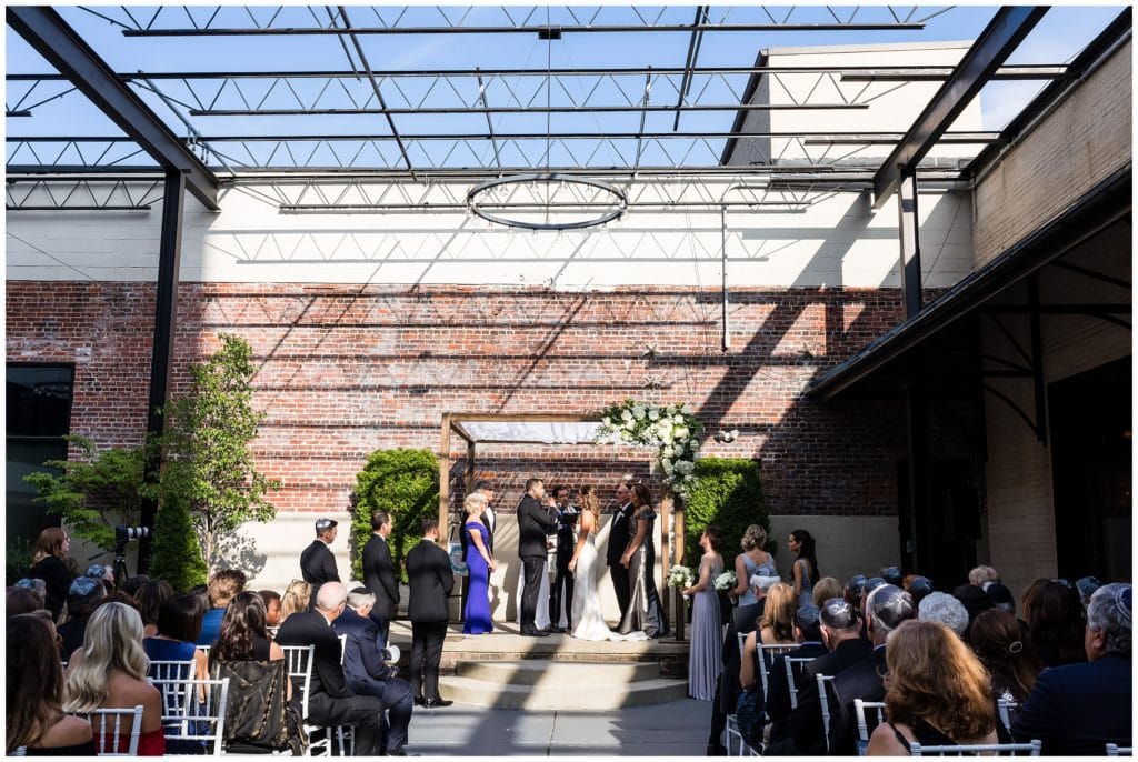 Vie courtyard Jewish wedding ceremony under chuppah with white florals and greens