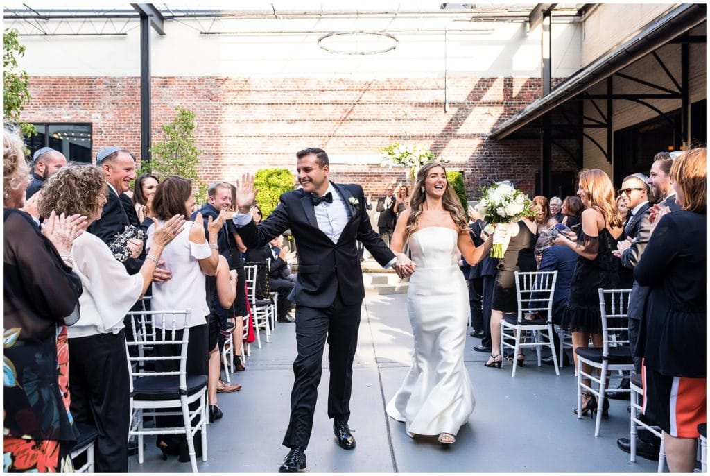 Bride and groom walking up aisle, cheering and high-fiving guests