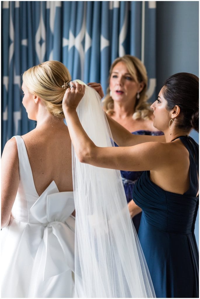 Bridesmaid attaching veil to hairpiece, big bow wedding gown