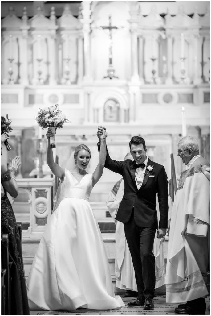 Black and white portrait of bride and groom cheering as they walk up the aisle after St. Augustine wedding ceremony