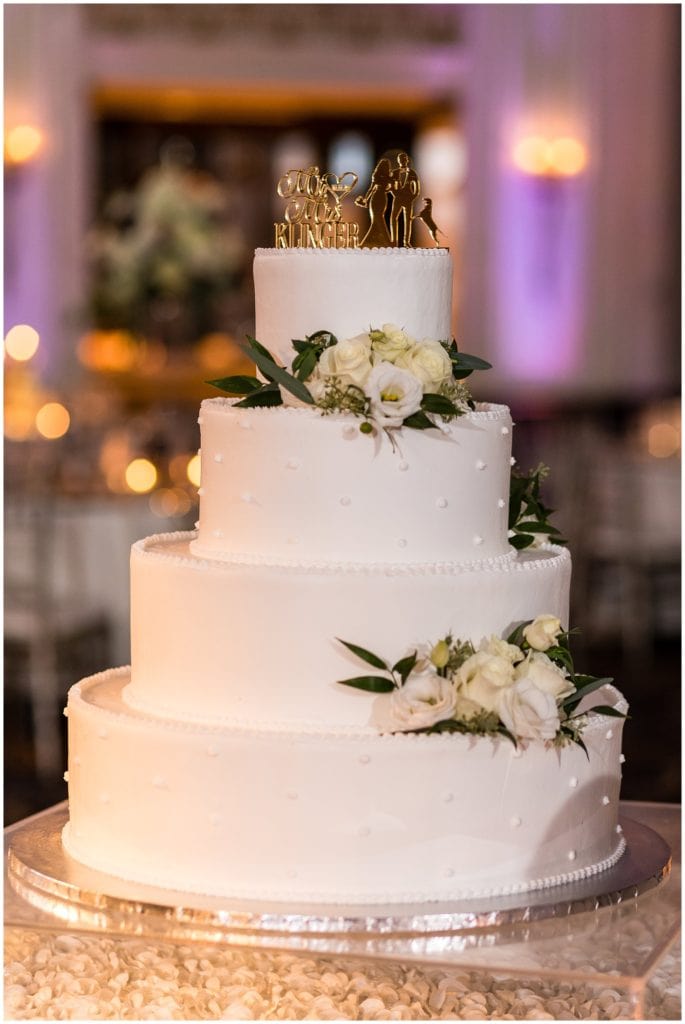 Elegant wedding cake with white florals and custom gold name cake topper