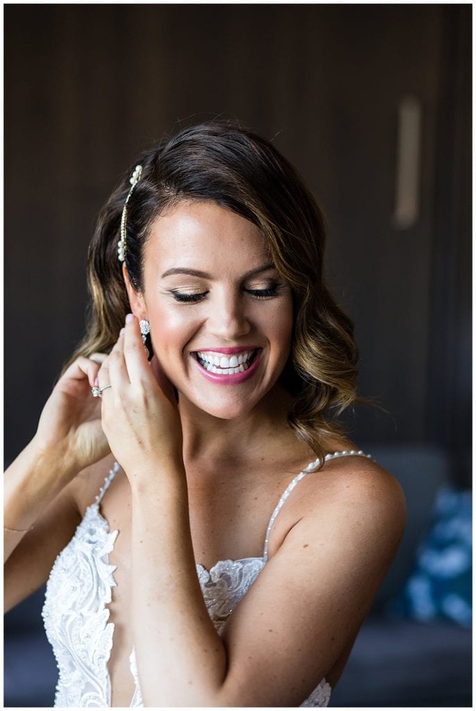 Window lit bridal portrait of bride putting on her earrings