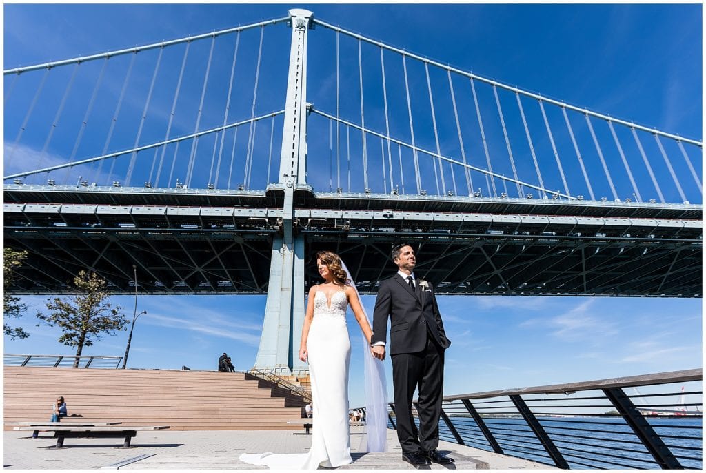 Bride and groom pose in front of bridge at Race Street Pier, Philadelphia wedding portrait
