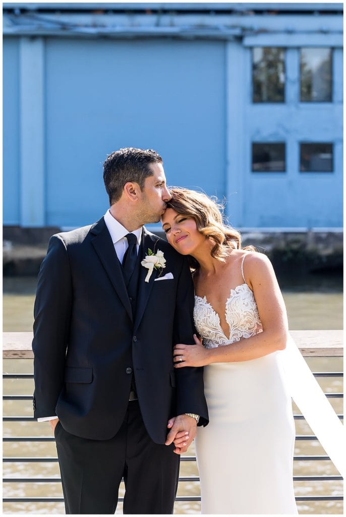 Groom kissing bride on the forehead on Race Street Pier in Philadelphia