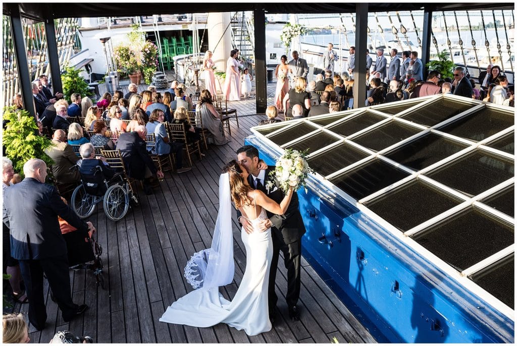 Bride and groom kiss at the end of the aisle on the Moshulu boat, full ceremony with guests in Philadelphia wedding