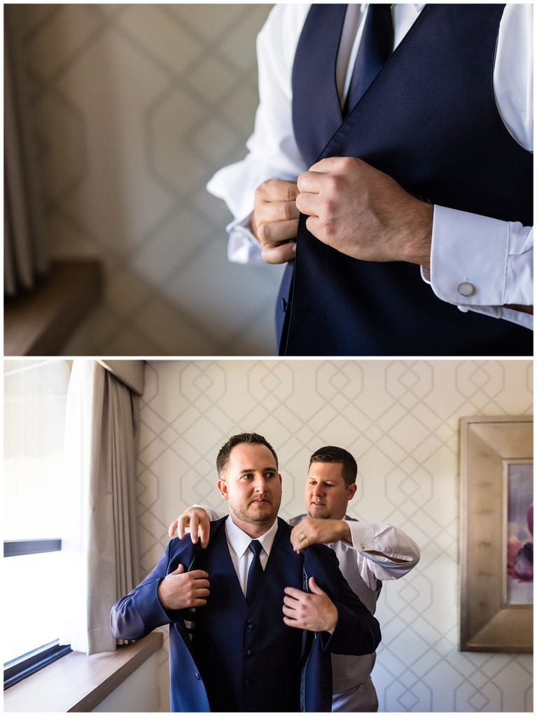 Groom putting on his vest and jacket with help from groomsmen