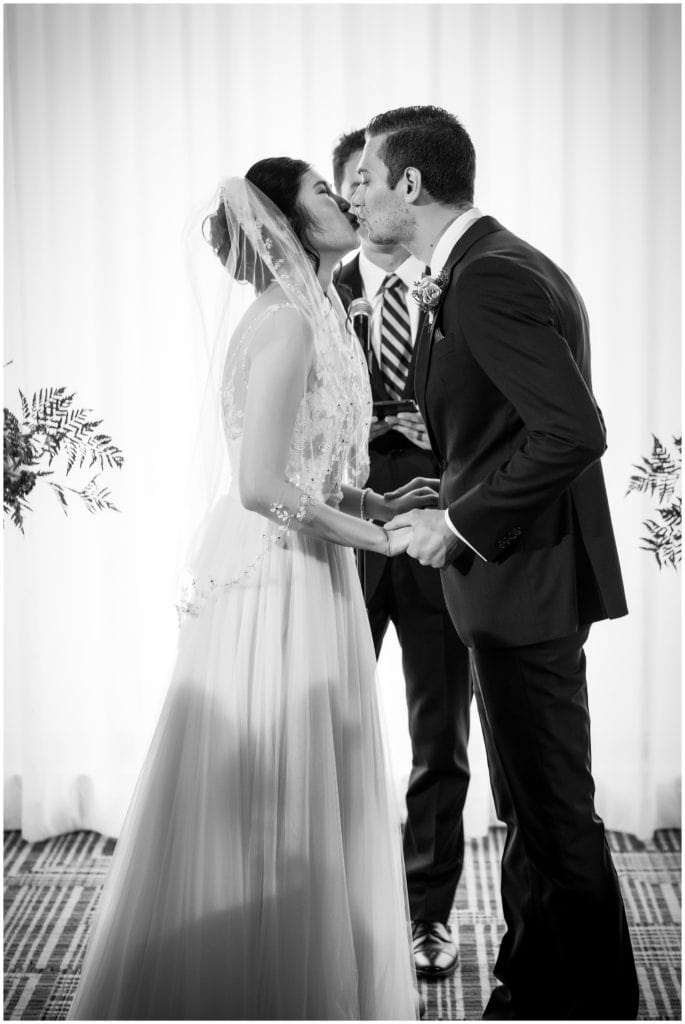 Black and white portrait of bride and groom kissing during wedding ceremony