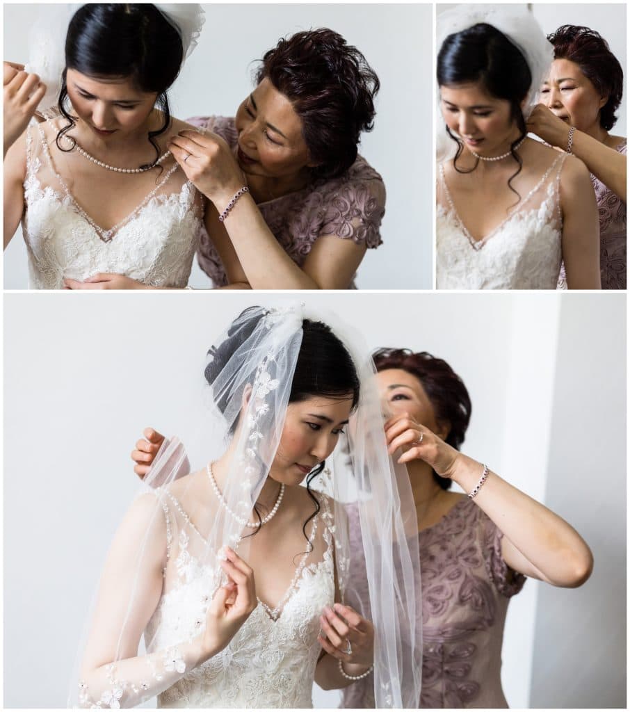 Mother of the bride helping bride put on her necklace and veil