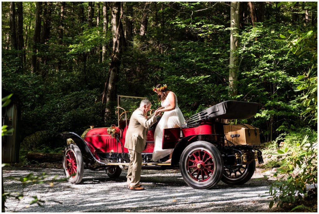 Father of the bride helping bride out of classic car at wedding ceremony