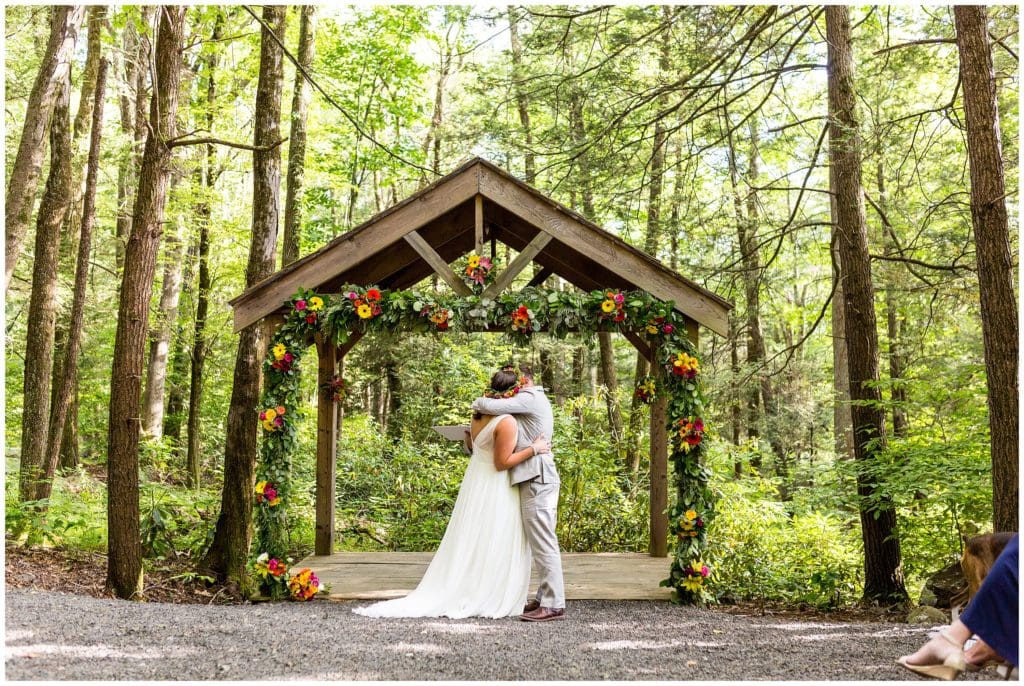 Bride and groom kiss during woodsy outdoor wedding ceremony