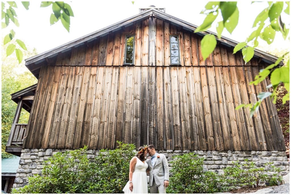 Bride and groom softly embracing in front of woodsy barn venue