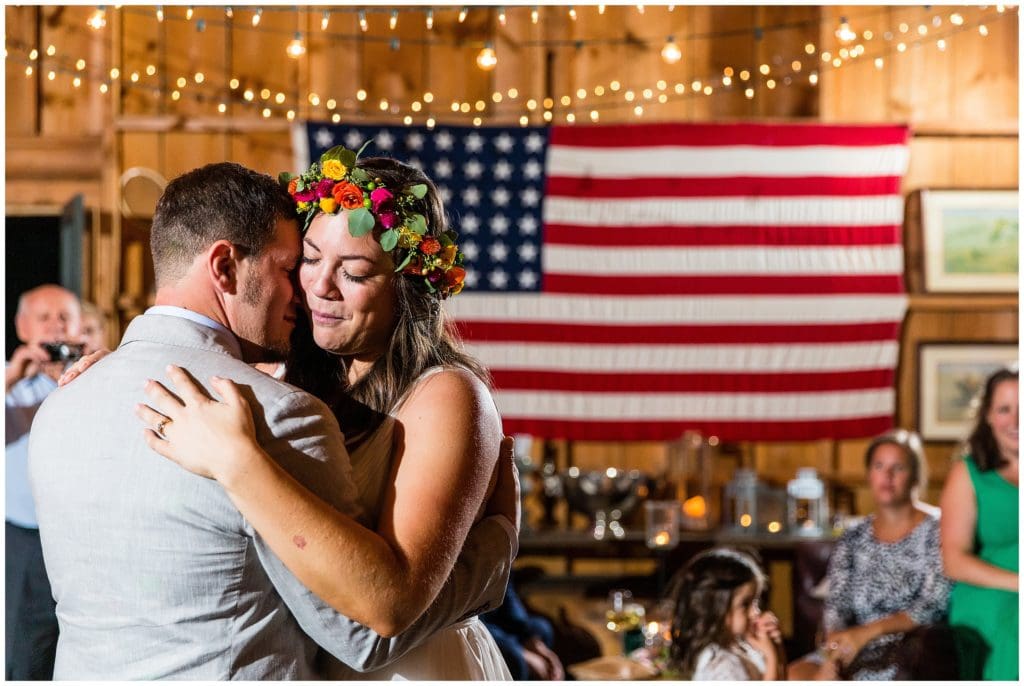 Romantic portrait of bride and groom sharing first dance with American flag and string lights in background
