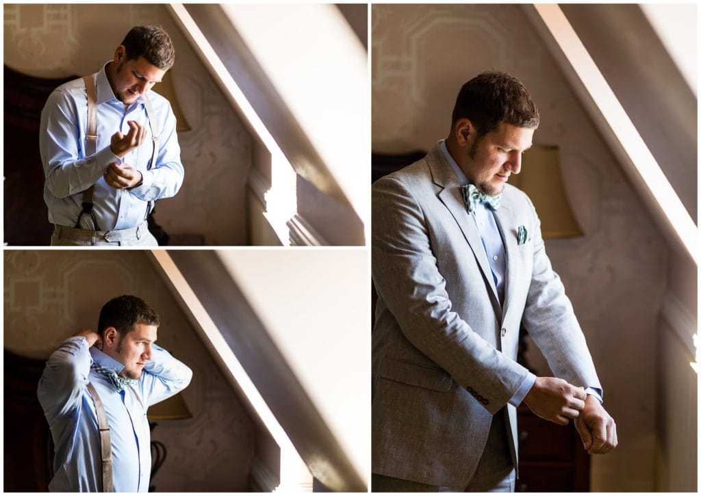 Traditional window lit groom portraits of groom tying tie and putting on jacket