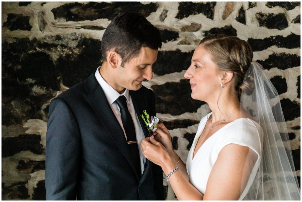 Bride looking at and pinning boutonniere on groom